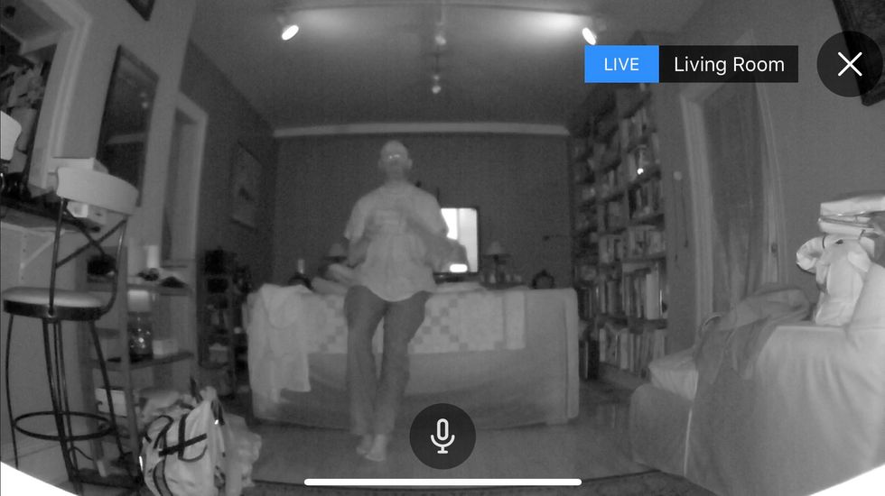 A black and white image taken through a security camera of a man in a room surrounded by furniture and books