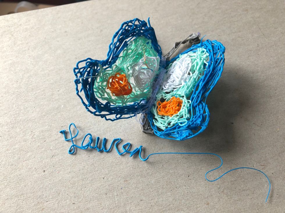 A butterfly with orange and white spots on its wings, draw in light and dark blue plastic threads