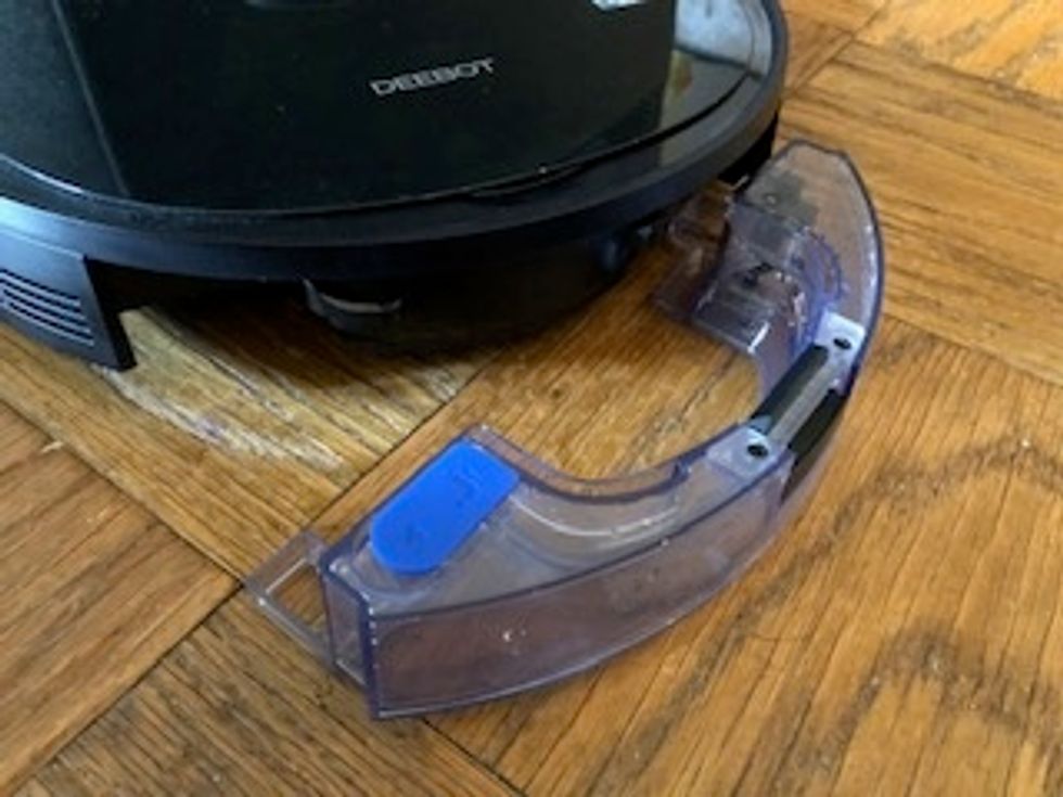 A clear plastic bin pulled out of a robot vacuum on a wood floor
