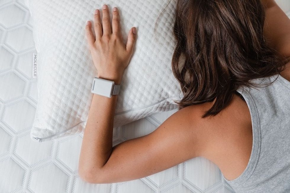 A figure face down, asleep in a bed with a white bracelet on the wrist