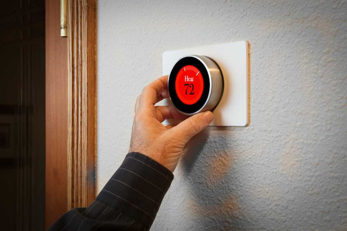 A hand adjusting a smart thermostat on a wall
