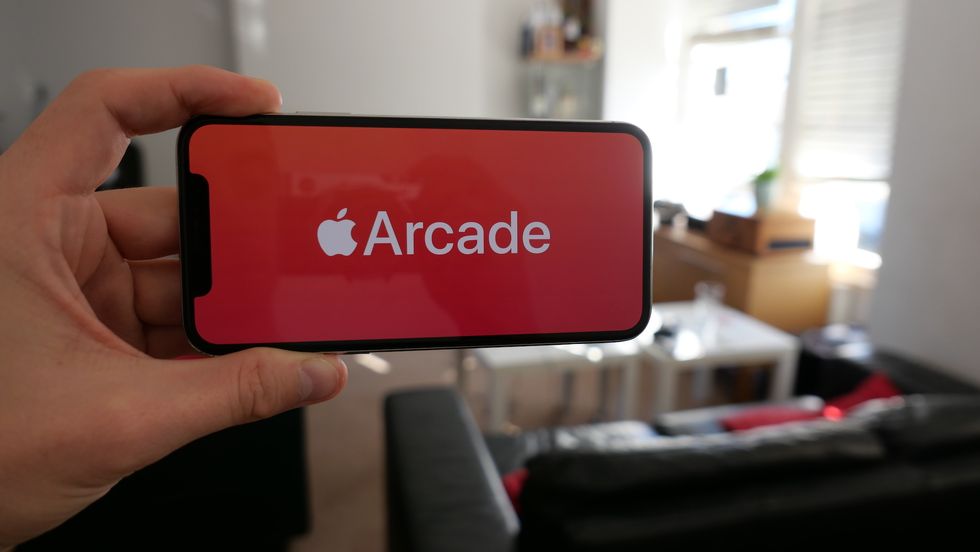 A hand holding an iPhone with the word Arcade written on the screen with a red background