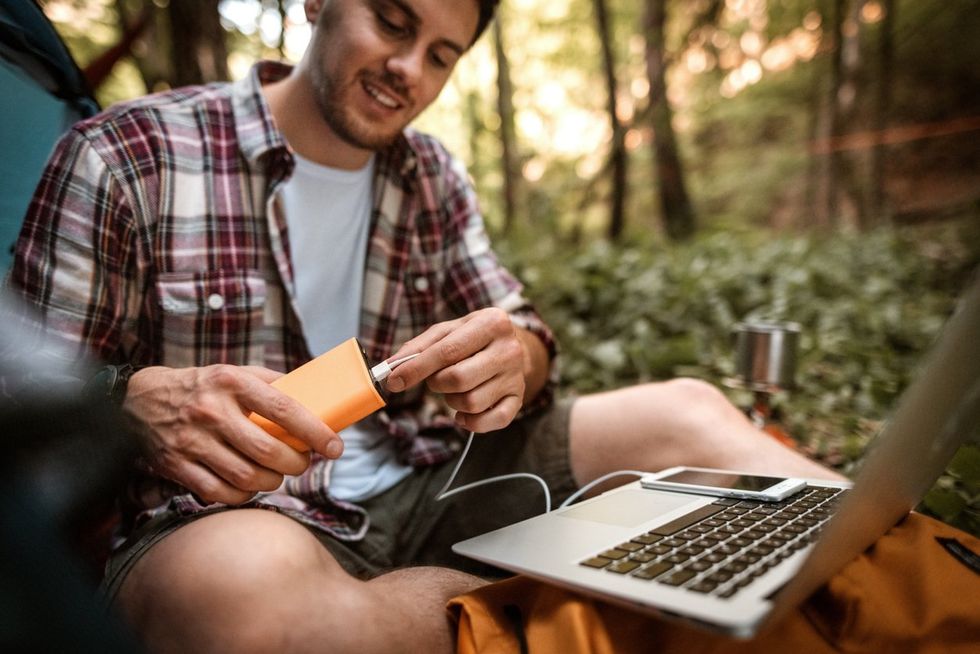 a man camping and using power bank to keep his phone and computer powered.