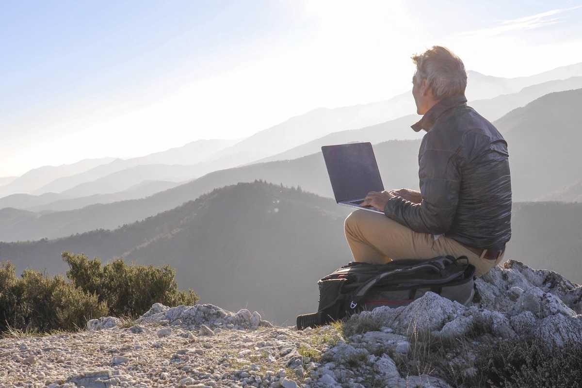 a man sitting outside with his computer looking at the mountains.