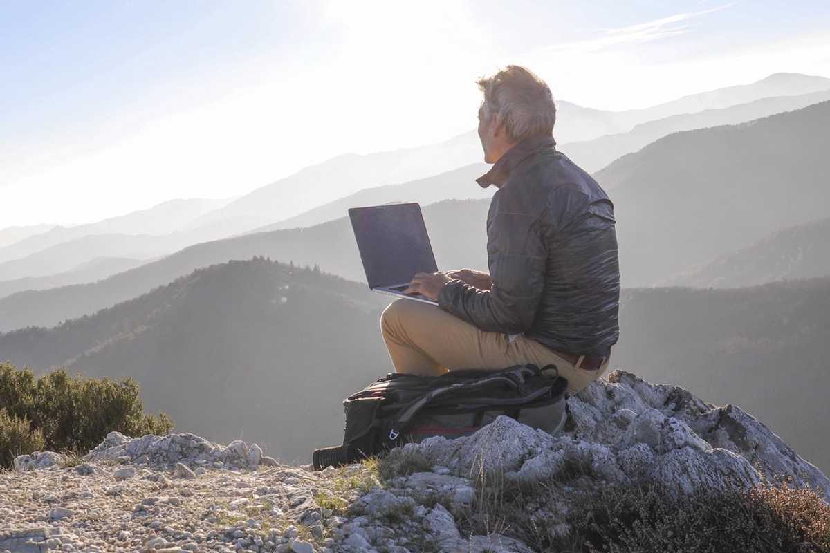 a man sitting outside with his computer looking at the mountains.