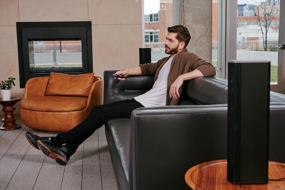 a man watching TV in a room with Enclave Audio speakers