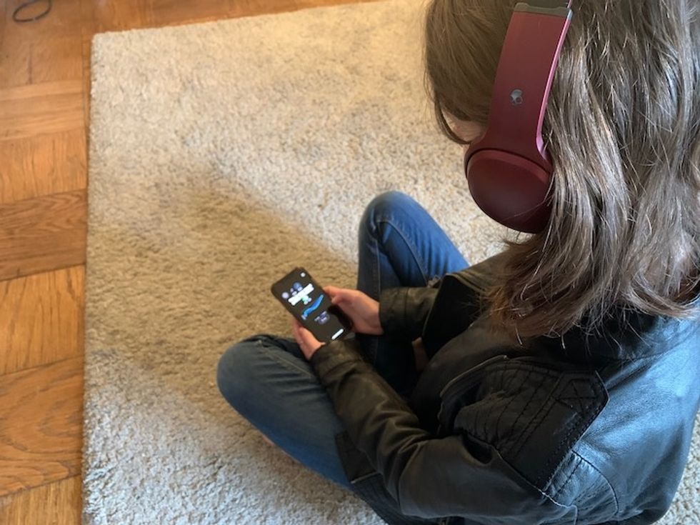A person wearing the red Crusher ANC headphones seated on the floor and holding a smartphone