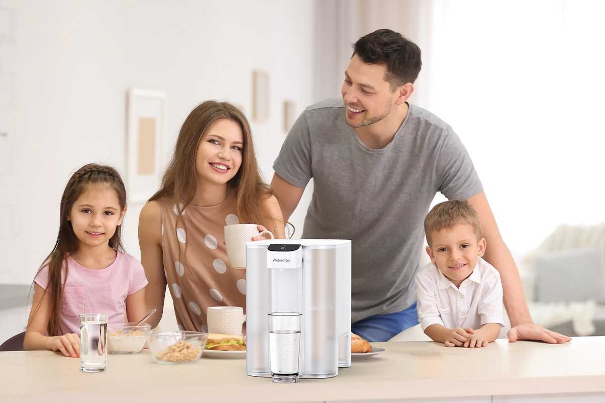 a photo of a family around a counter with the Waterdrop Mega Electric Water Filter Pitcher and glasses of water