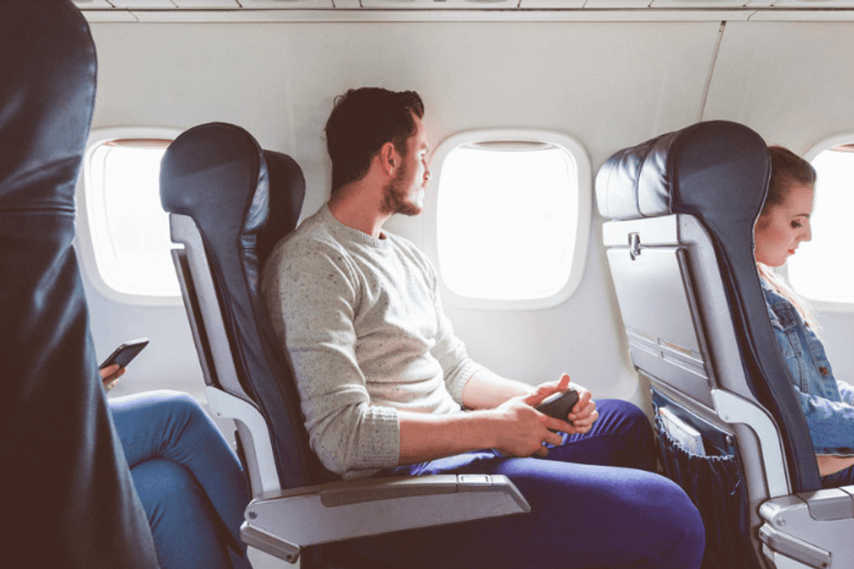 a photo of a man sitting on an airplane with cellphone in his hand.