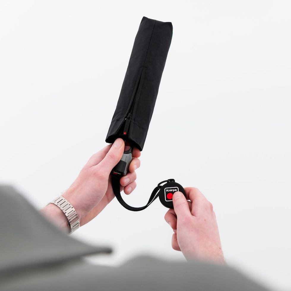 a photo of a person holding a Knirps\u2019 popular umbrella with Chipolo attached to it.