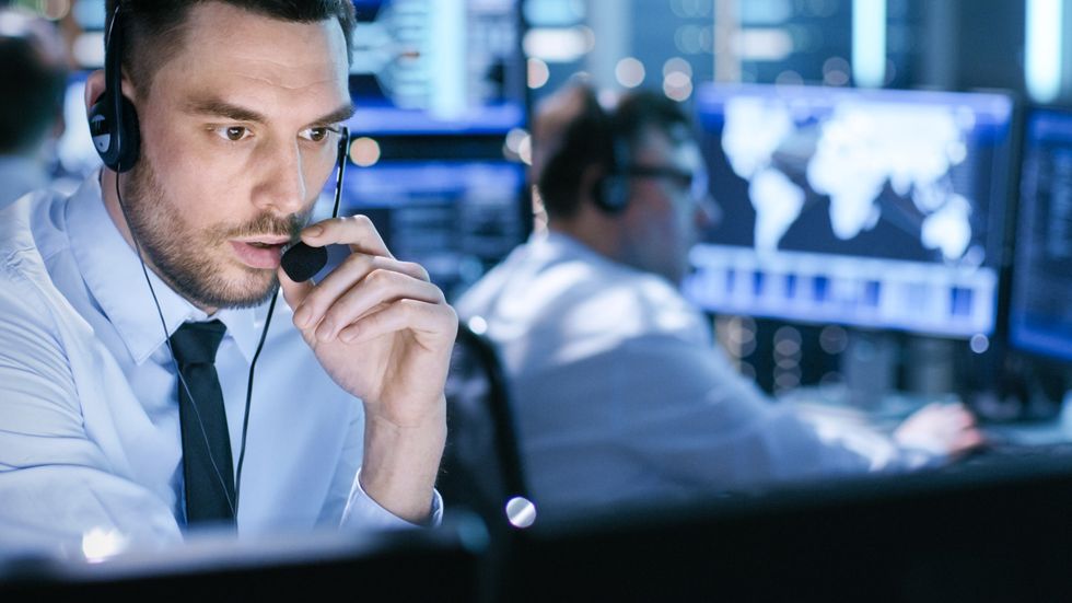 A photo of a professional monitoring security person on the phone in front of a computer