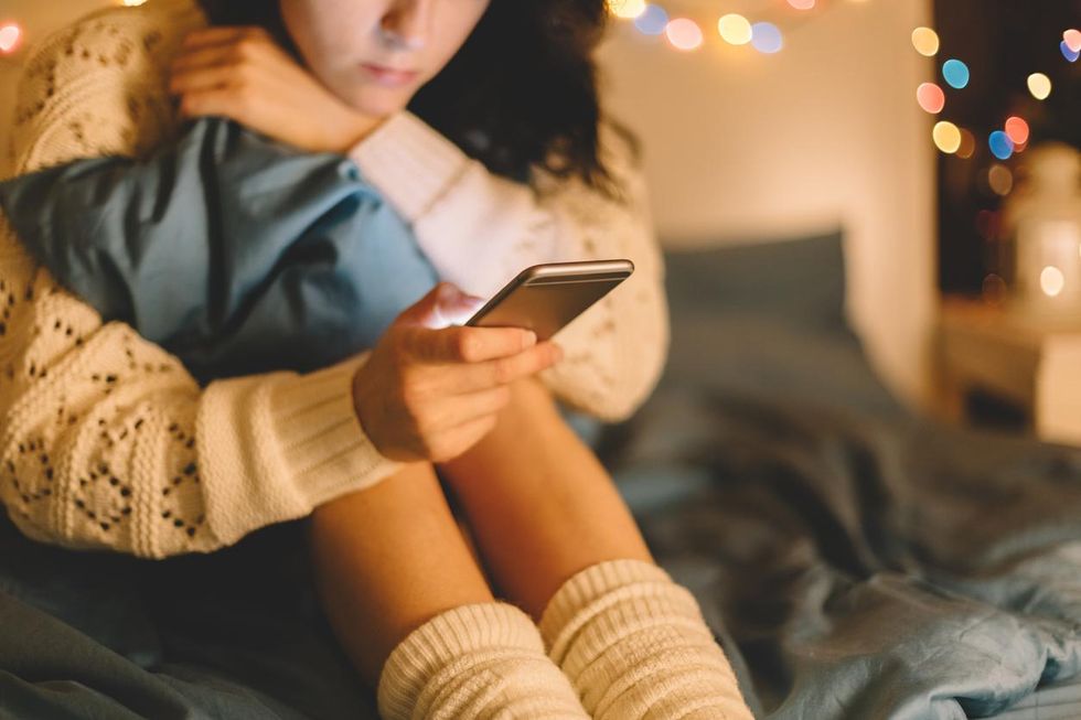 a photo of a woman in bed staring at her smartphone.