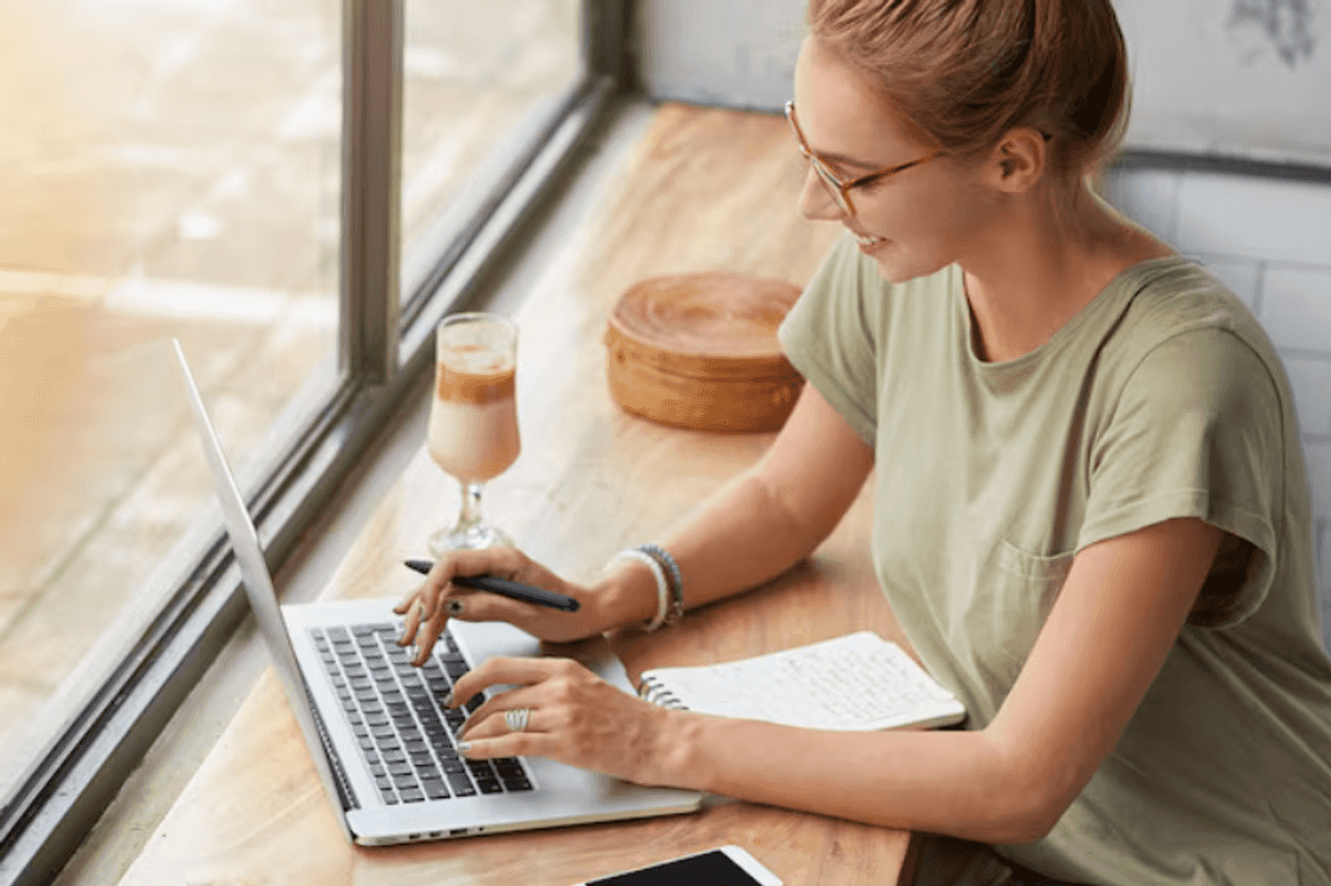 a photo of a woman typing on a laptop by a window