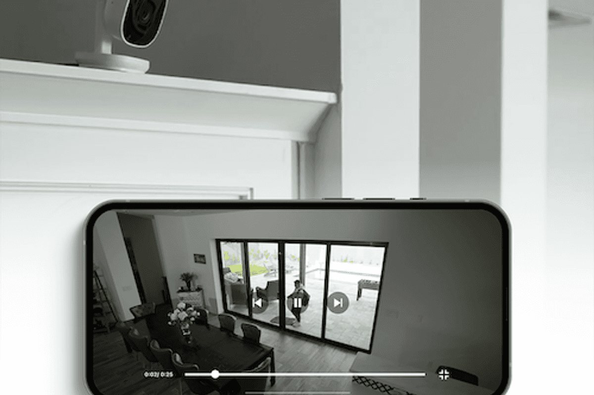 a photo of the myQ Smart Indoor Camera on a mantal and a smartphone showing live feed from the indoor camera in the myQ app.