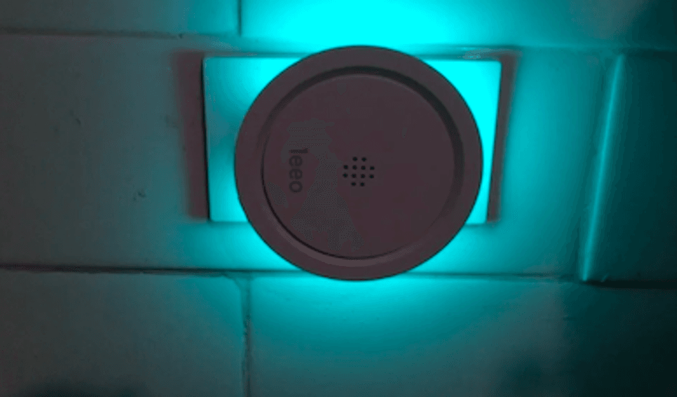 A round device from Leeo against a white wall with a blue light surrounding it