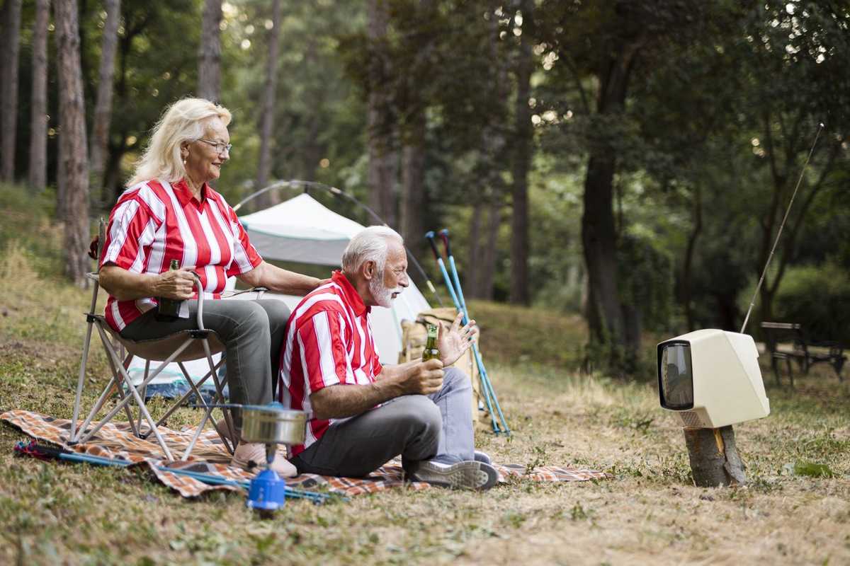 a senior couple watching TV while sitting in their campsite.