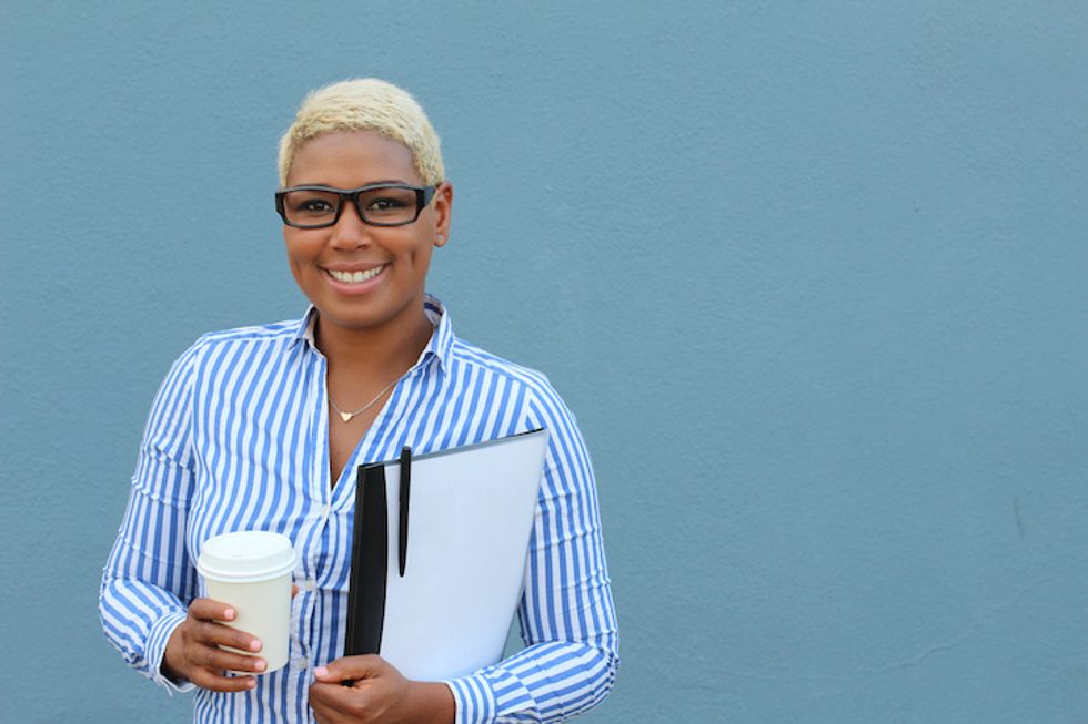 A teacher, smiling, holding a coffee and papers