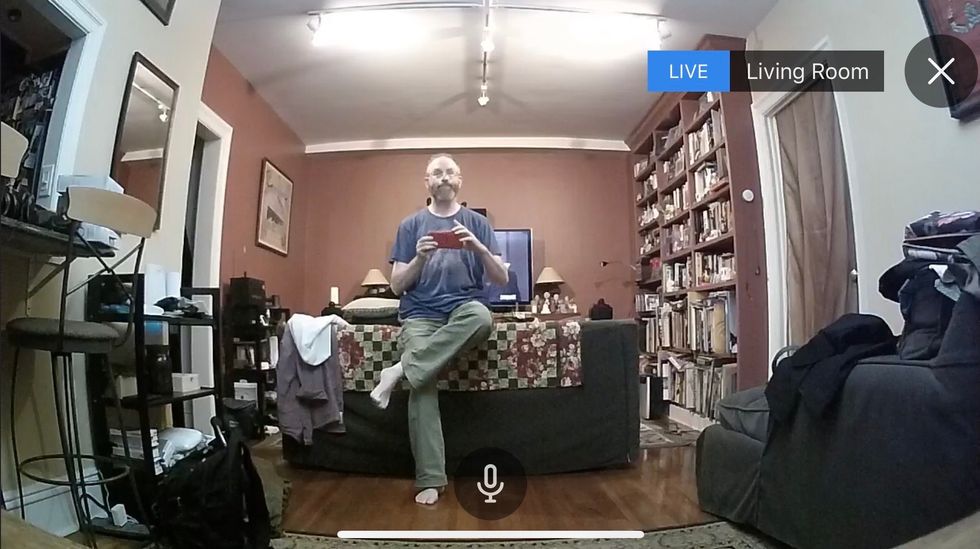 A view of a man in a living room through a security camera lens, surrounded by furniture and books
