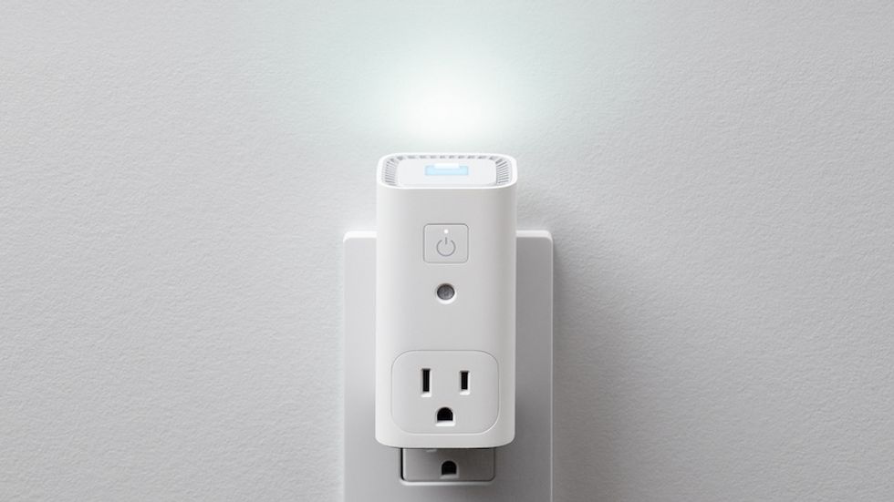 A white rectangular device plugged into an wall outlet, with a separate outlet, a power button, and a light illuminated at the top
