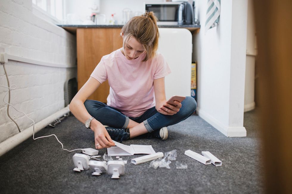 A woman in a pink T-shirt and jeans seated on the floor flipping through an instruction manual with three small security cameras in front of her