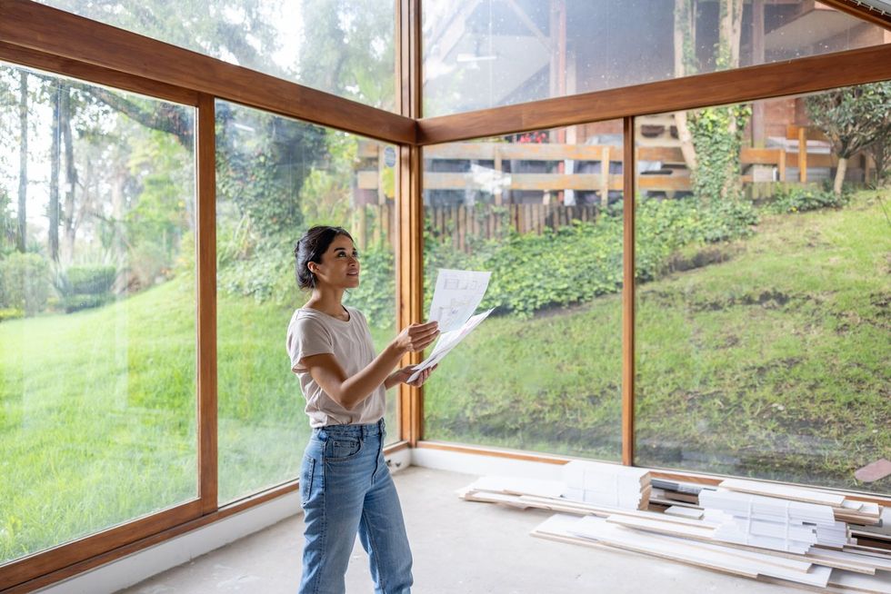 a woman looking at design plans infront of a wall of windows in a home that is being renovated