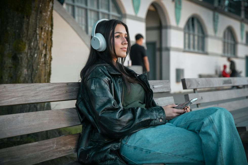 a woman wearing headphones while sitting on a park bench