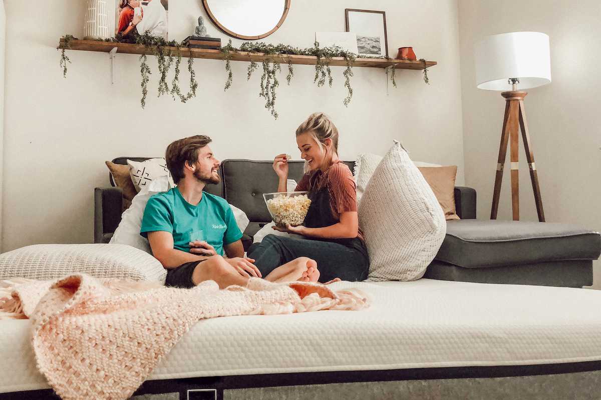 A young couple eats popcorn on a white bed