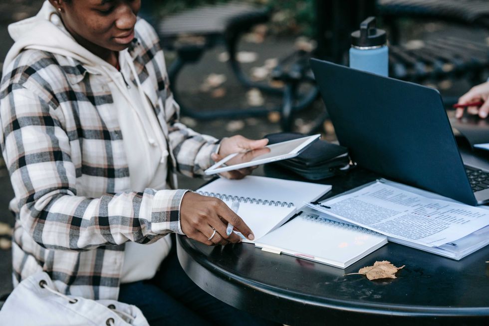 A young woman focusing on her studies outdoors with a laptop and notebook.
