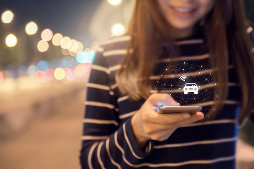 A young woman holding a smartphone hailing a ride through an app
