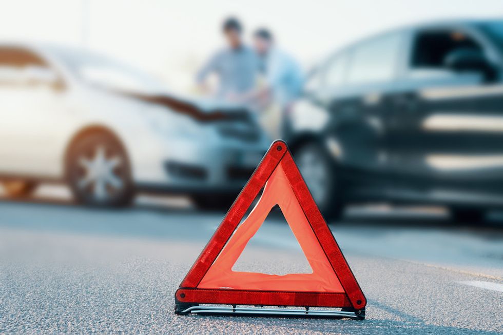 An orange traffic triangle in front of two cars, one with the hood damaged, and two figures talking