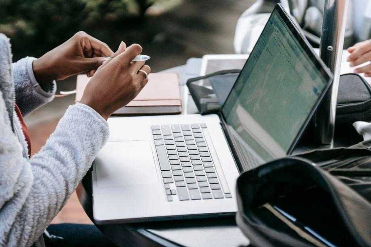 Close-up view of people working collaboratively with laptops and notebooks at an outdoor table.