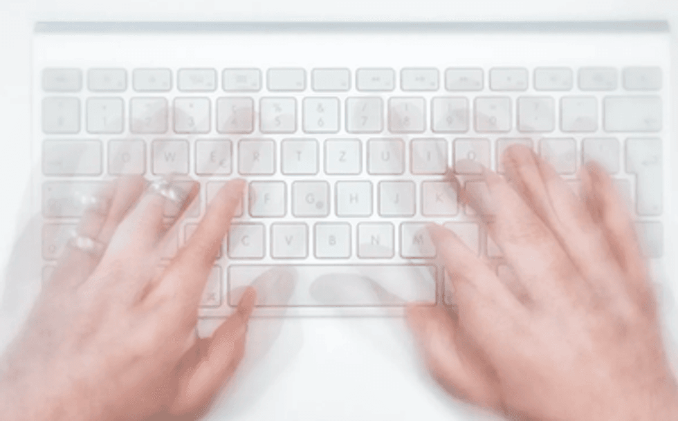 Hands typing on a white laptop