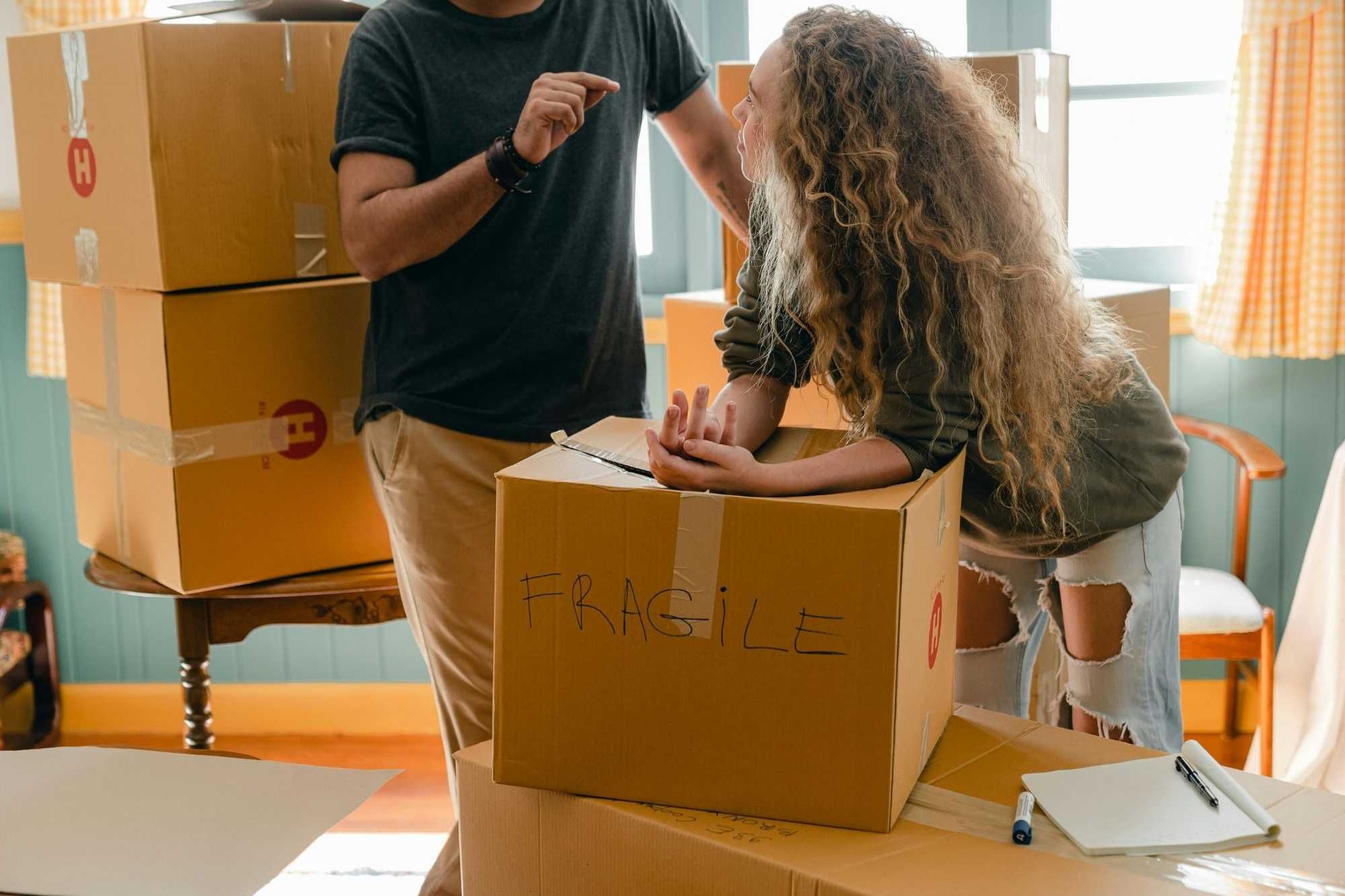 a girl leaning on a box marked fragile speaking with a mover.