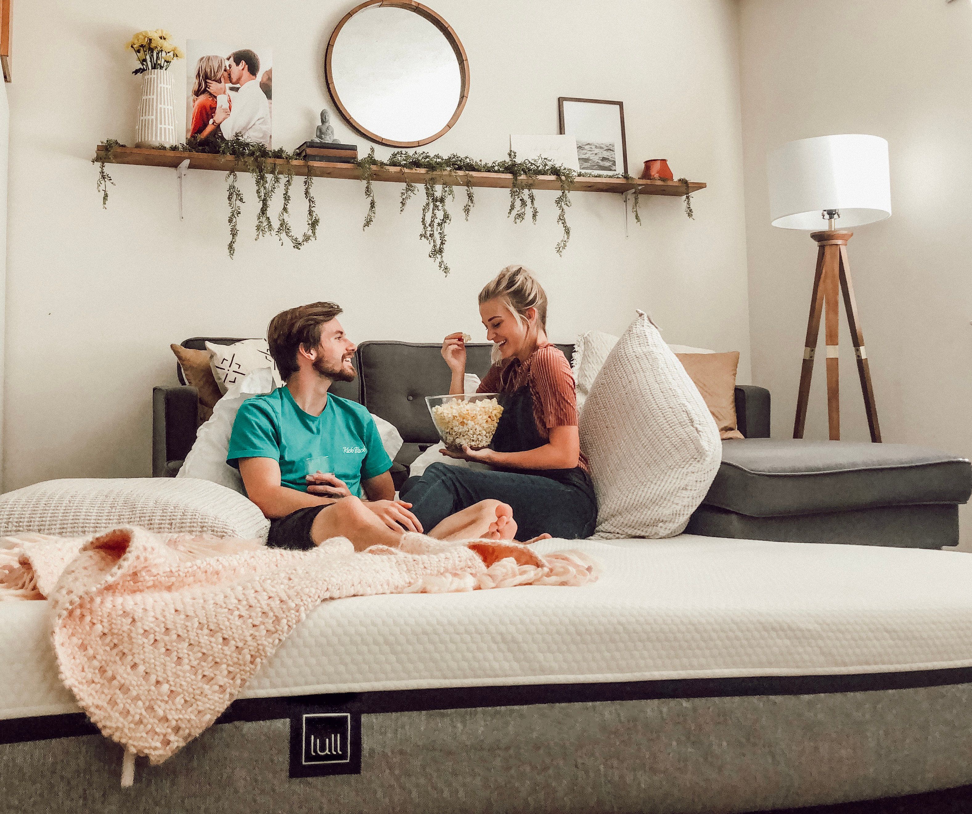 A young couple eats popcorn on a white bed