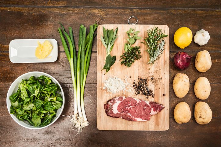 raw meat and vegetables on a wooden chopping board