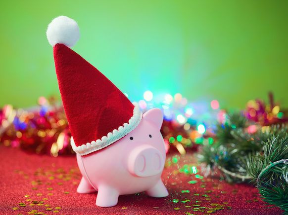 A pink piggy bank with a red Santa hat, with holiday decorations and green trees behind