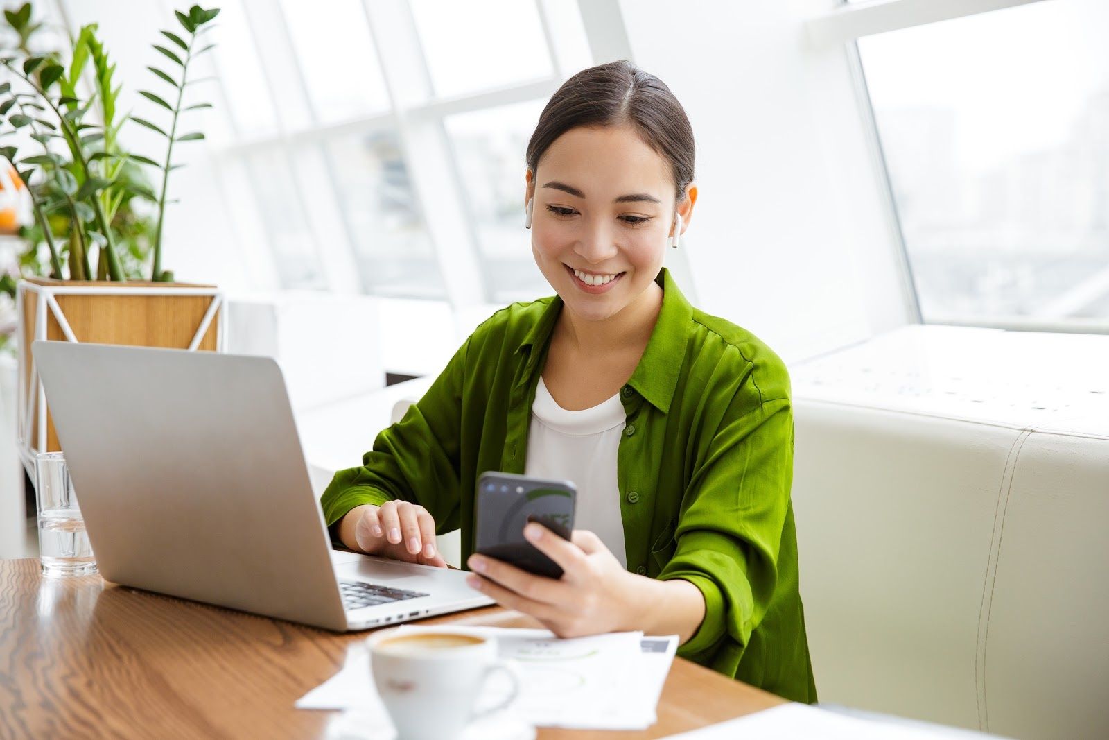 woman sitting down with laptop looking at her phone smiling