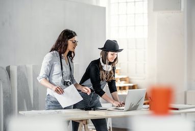 Two women working together on a creative project on their computer