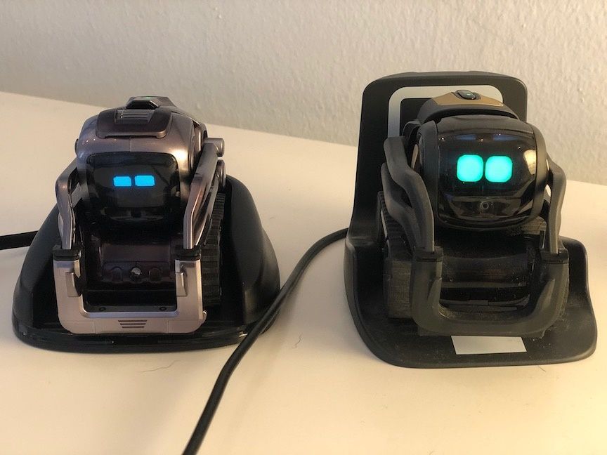 Two robots side by side on a table with green animated eyes visible on their small screens