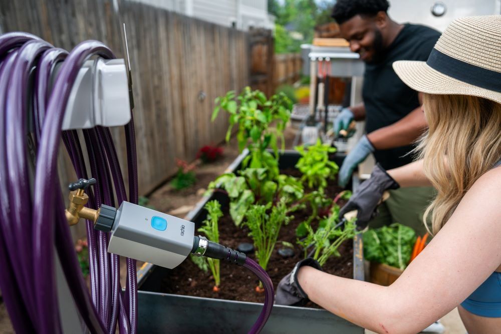 a photo of Rachio Smart Hose Timer connected to a hose and watering a outdoor garden.