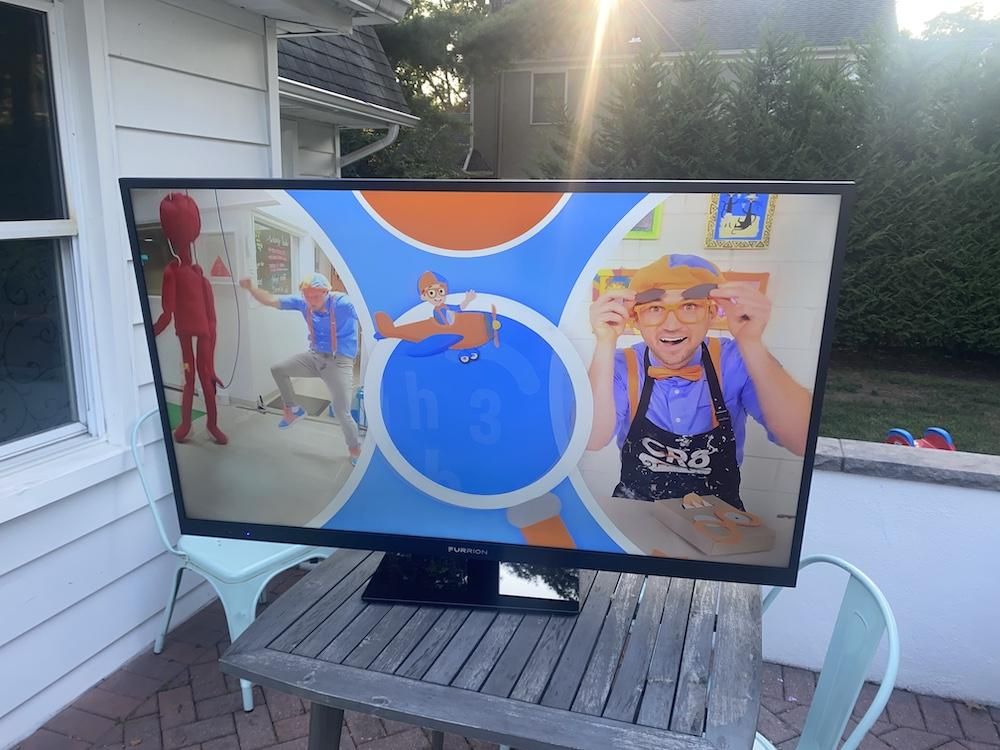 a photo of Furrion Aurora Full Sun Smart 4K UHD LED Outdoor TV on a table in a backyard.