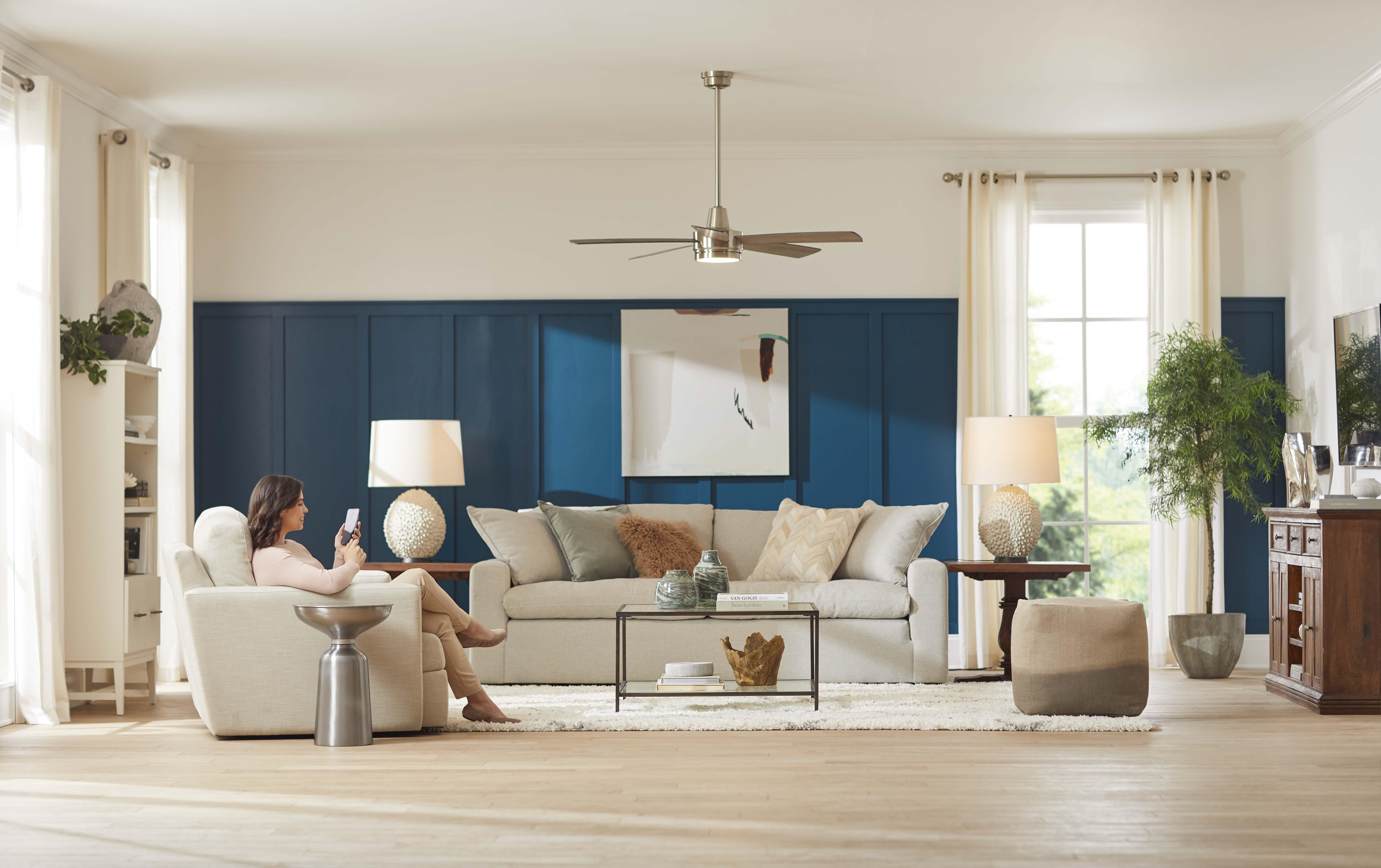 Living room with woman on smartphone controlling her fan with Hubspace app