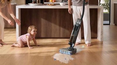 photo of a mom vacuuming up spilled milk on a wood floor using Roomba Electro Plus while her baby watches.