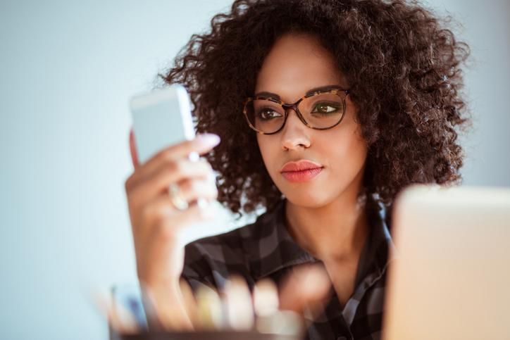 A woman holding a mobile device in front of a computer