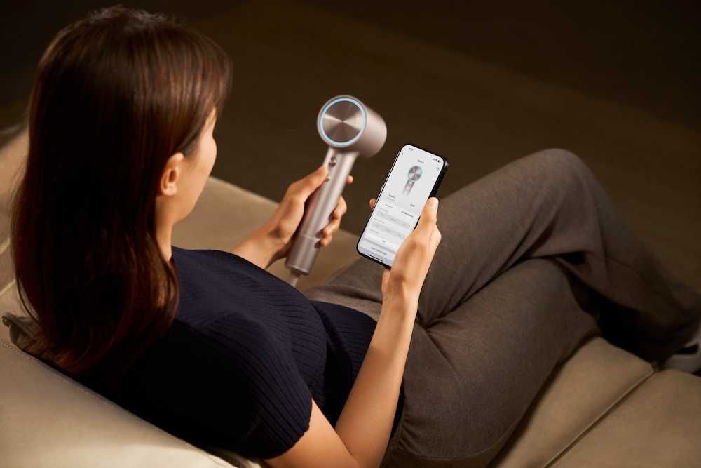 a photo of a woman using the app for the Laifen smart hair dryer while sitting on a couch