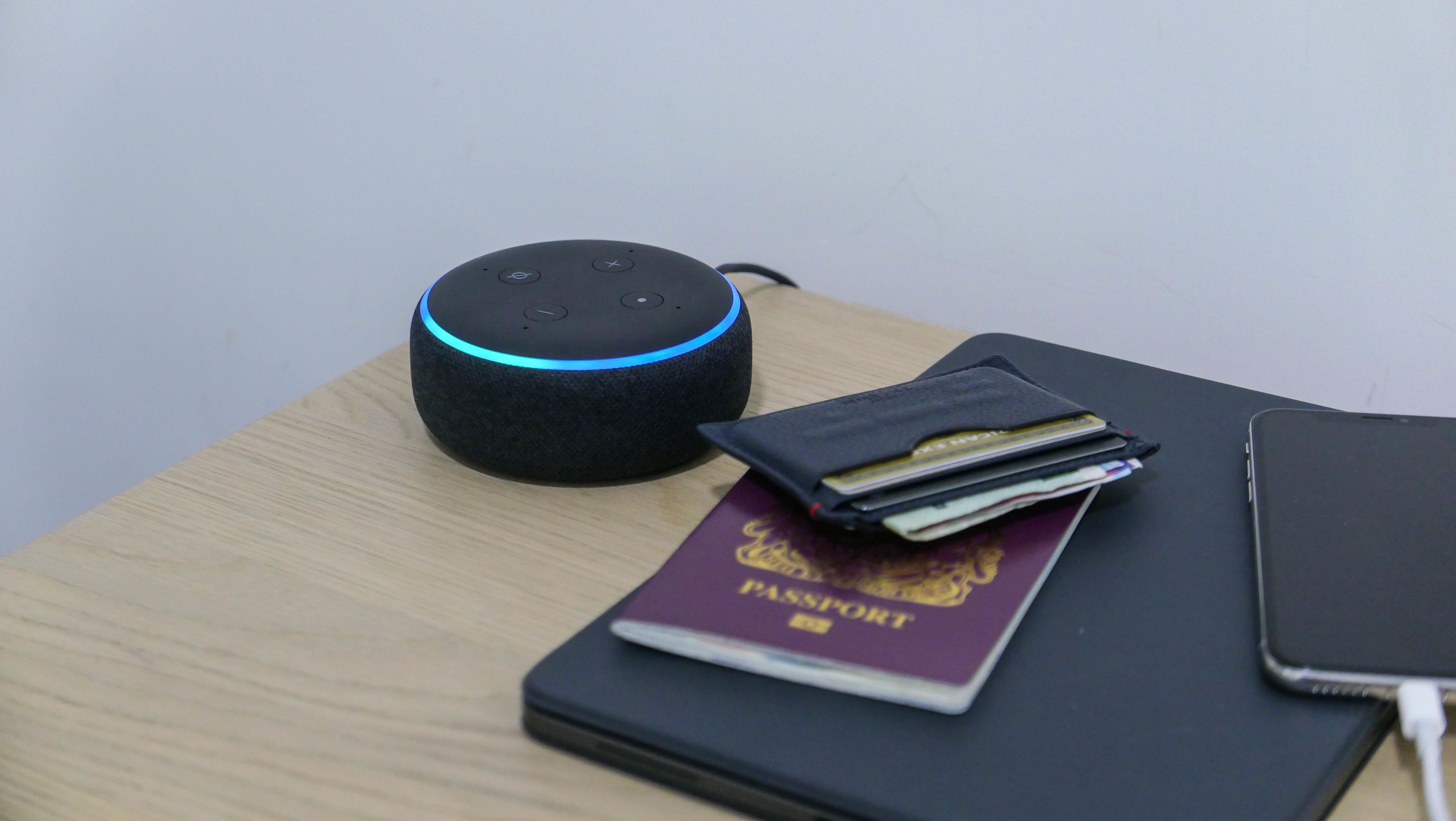 a picture of Amazon Echo Dot on a hotel beside table next to passports and a wallet.