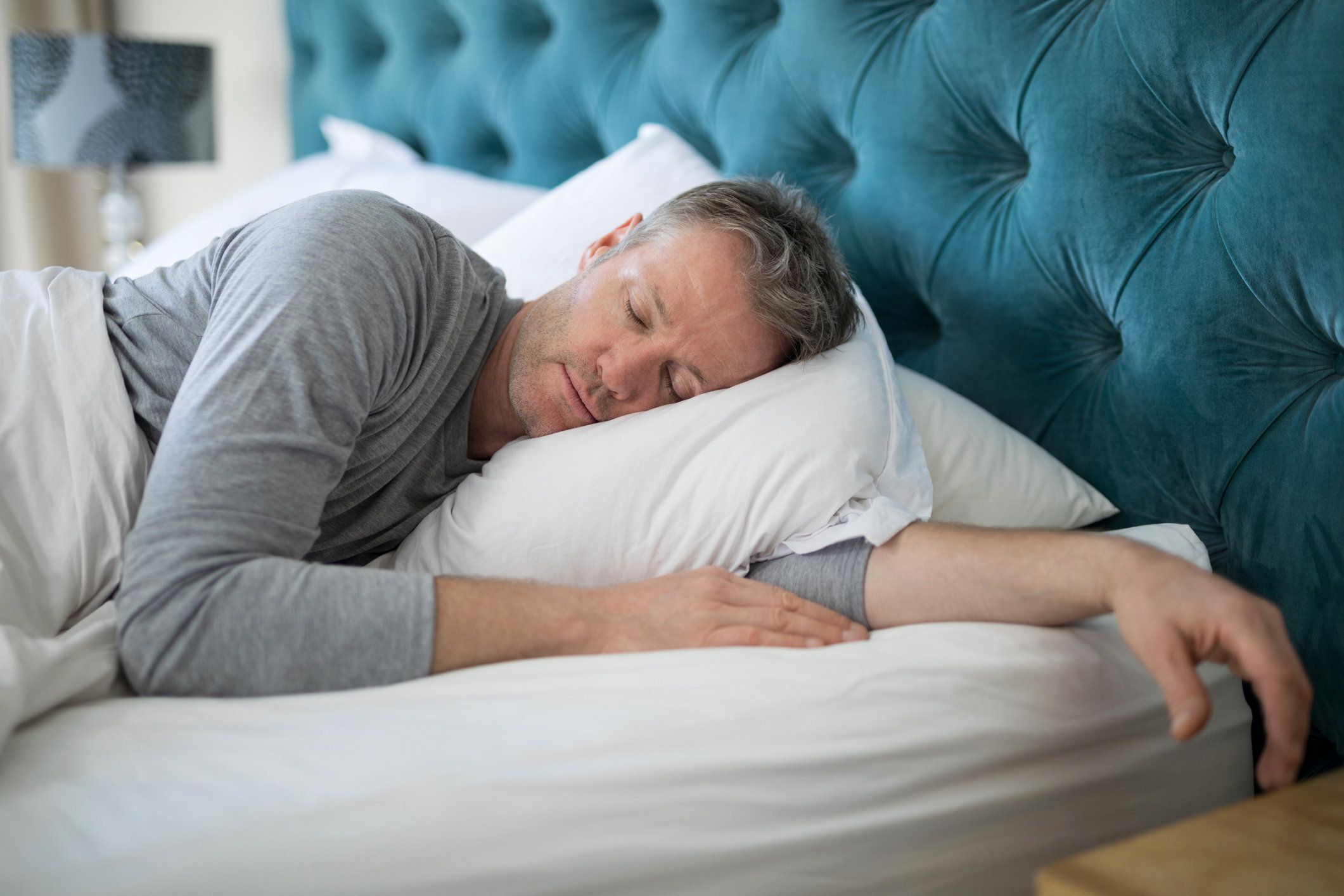 A man sleeping on a bed listening to Google Assistant play sounds on a smart speaker.