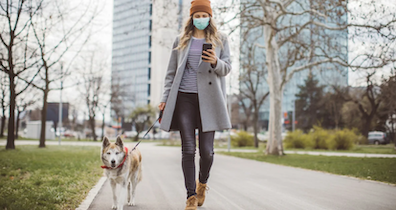 A woman walking a dog on her mobile phone with a mask