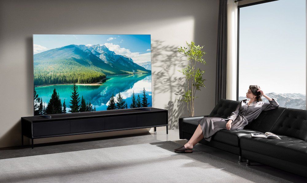 Photo of TCL AM8K Smart TV on a entertainment center in a room with a woman sitting on the couch watching tv