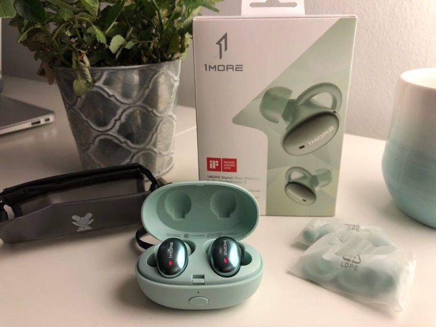 A pair of mint green 1More Stylish True Wireless In-Ear Headphones in the matching green case on a white table